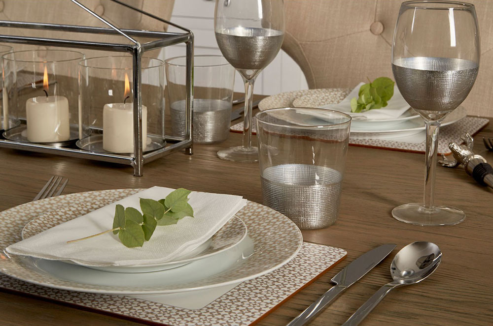 Modern, ezüstszínű fémmel díszített, röviditalos és boros üveg poharak, terített ünnepi asztalon.