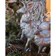 Glamour stílusú, 21 cm magas, ezüst színű karácsonyi szarvas figura 3 változatban fenyők és tobozok között