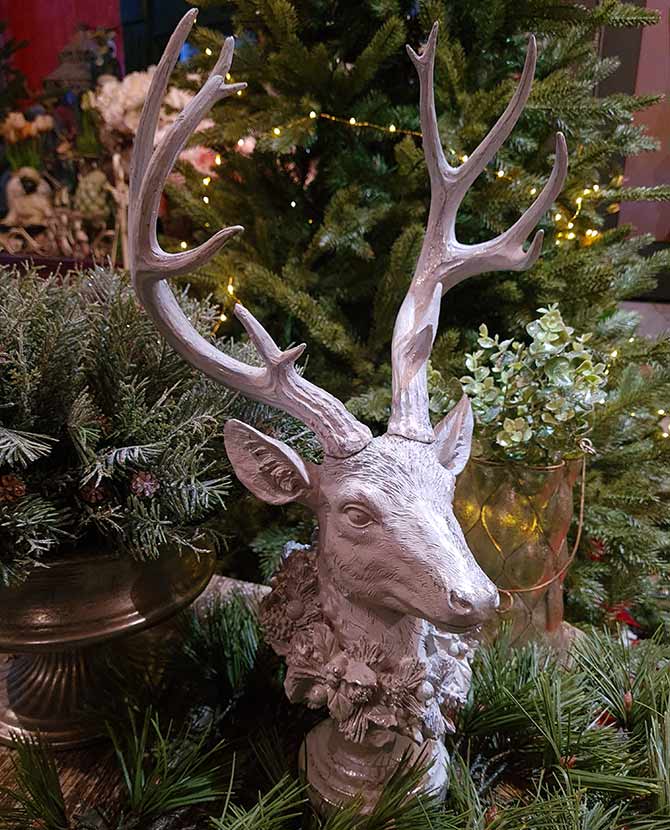 Prémium kategóriás, részletgazdagon kivitelezett glitteres karácsonyi szarvas koszorúval a nyakában fenyők között 