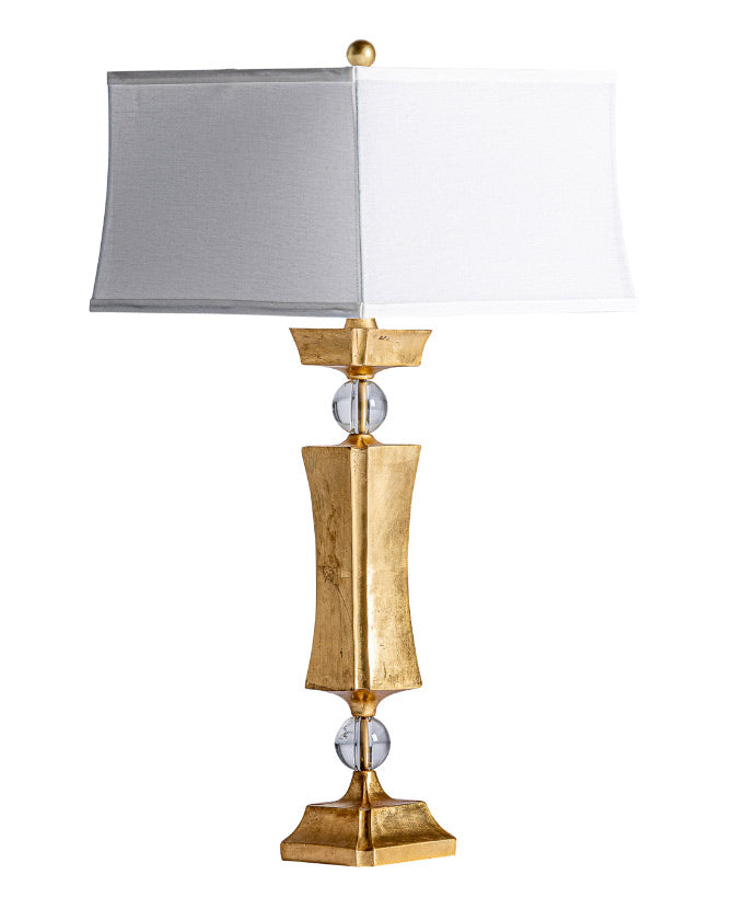 Art Deco stílusú, dekoratív formájú, fémből készült, arany színű dizájn asztali lámpa fehér színű, lenvászon lámpaernyővel.