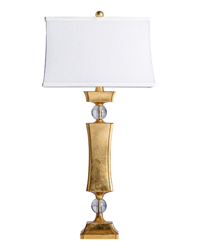 Art Deco stílusú, dekoratív formájú, fémből készült, arany színű dizájn asztali lámpa fehér színű, lenvászon lámpaernyővel.