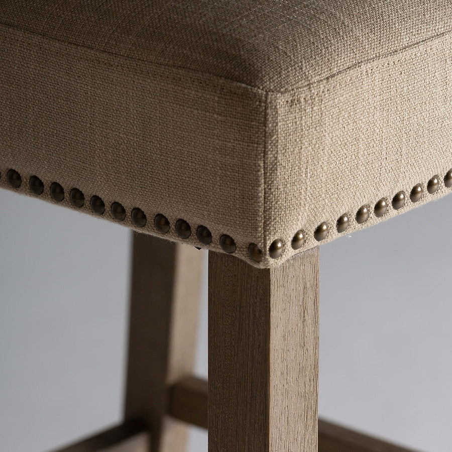 A koloniál stílusú bárszék lábrészlete a vászonkárpittal és az antikolt szegecsekkel.