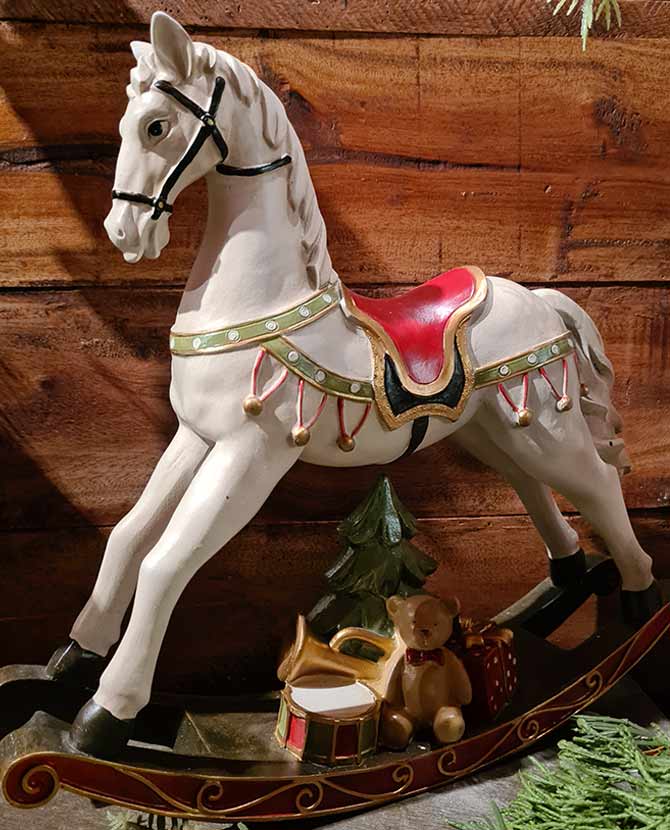 Vintage stílusú, 29,5 cm hosszú, fehér és piros színű karácsonyi hintaló ajándékokkal barna deszkafal előtt