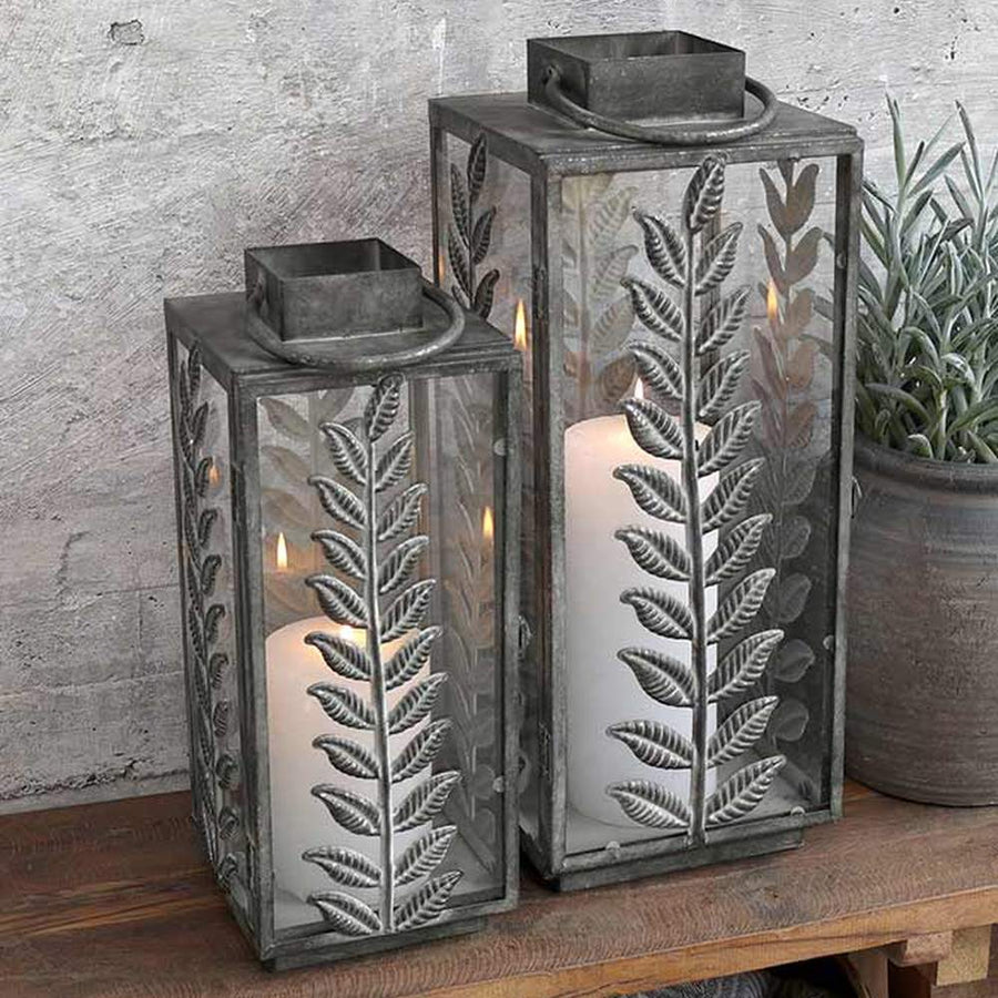 Kültéri konzolasztalon álló vintage, fém lámpások, dekoratív levélmotívummal díszítve.