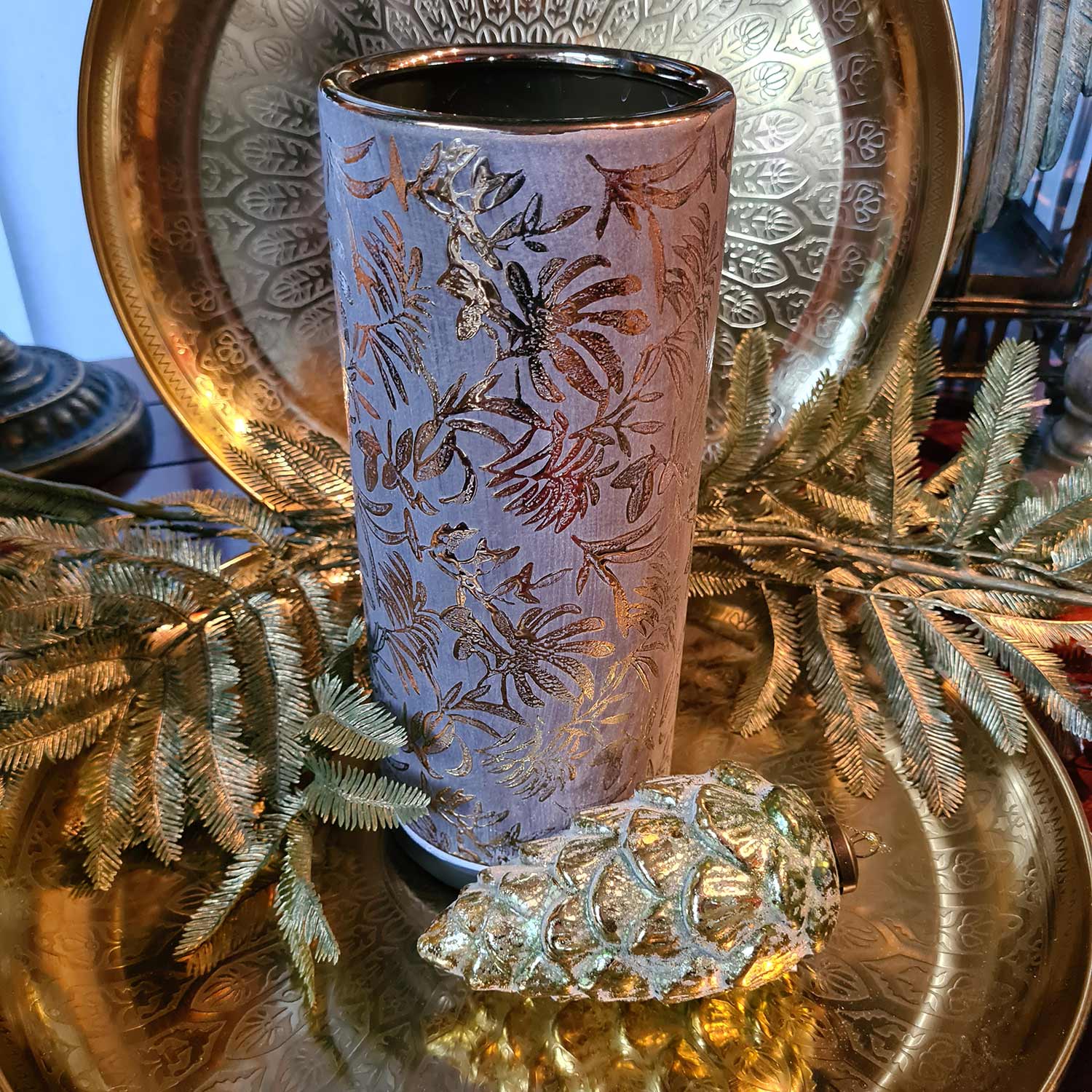 Aranyszínű dombormintával díszített, modern, glamour stílusú kerámia arany váza., aranyszínű fém tálcán, üveg tobozzal.