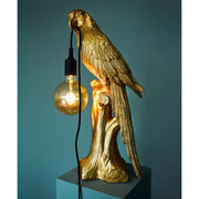 Aranyszínű papagáj figurás, 61 cm magas, trópusi, glamour stílusú asztali lámpa, szürkéskék háttér előtt.