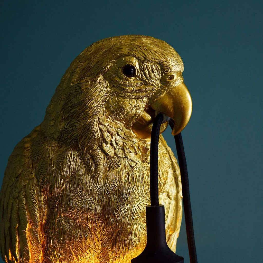 Arany színű papagáj, csőrében dekorfoglalat.