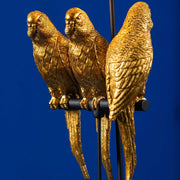 Aranyszínű papagáj figurákkal díszített, 79 cm magas, trópusi, glamour stílusú asztali lámpa, kék háttér előtt.