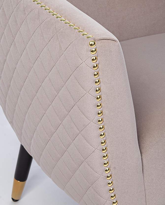 Glamour stílusú, bézs színű bársonyfotel aranyszegecsekkel díszített karfájának részlete.