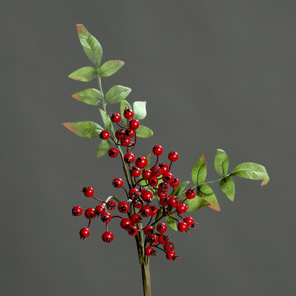 Mesterséges piros bogyós karácsonyi ág, hervadó zöld színű levelekkel.