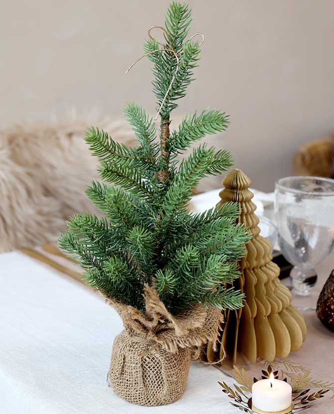 Karácsonyi asztalt díszítiő, élethű, kisméretű deko fenyőfa jutazsákban.