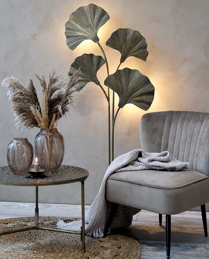Glamour stílusú szobában álló velúrfotel, kisasztal, háttérben a ginkgo leveles fém állólámpával.