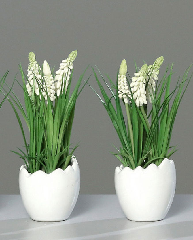 Krém színárnyalatú mű gyöngyike virág, tojás formájú, fehér színű kerámia kaspóban.