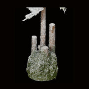 Havas felületű, 80 cm magas, mesterséges dekorációs műfenyőfa, mohával borított talapzatának közeli képe fekete háttér előtt