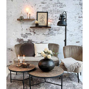 Ipari stílusú, antikolt fekete színű, fém állólámpa enteriőrben bútorokkal, fehér kopott téglafal előtt.