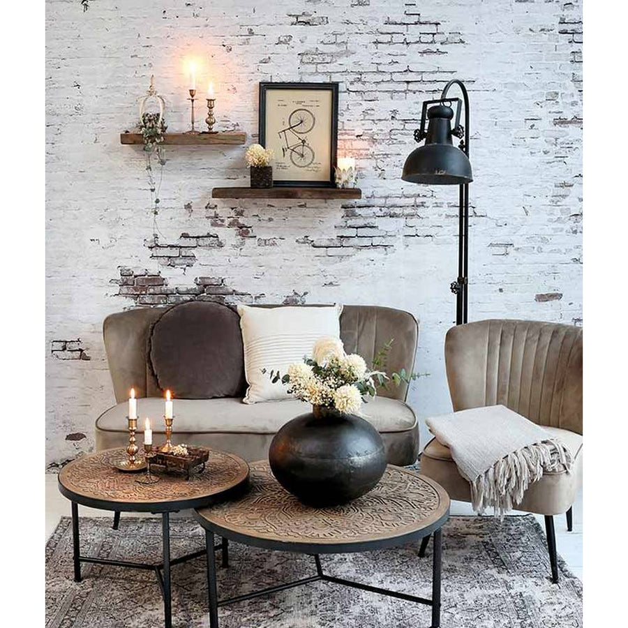 Ipari stílusú, antikolt fekete színű, fém állólámpa enteriőrben bútorokkal, fehér kopott téglafal előtt.