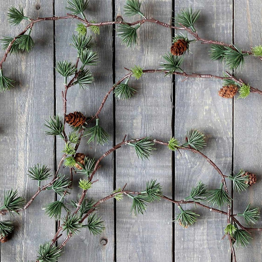 Tobozokkal díszített mű karácsonyi cédrus fenyő girland szürke színű deszka falon.