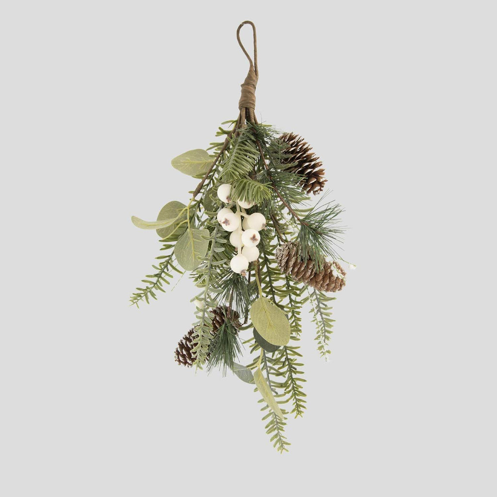 Eukaliptuszból, többféle fenyőágakból készült, fenyőtobozokkal és fehér bogyós terméssel díszített karácsonyi ajtódísz szürke háttér előtt.