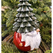 Karácsonyi manó fenyősapkában, zöld fenyők között.