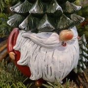 Karácsonyi manó fenyősapkában, zöld fenyők között.