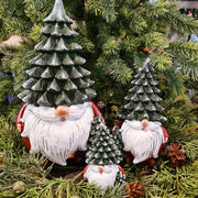 Karácsonyi manók fenyősapkában, zöld fenyők között.