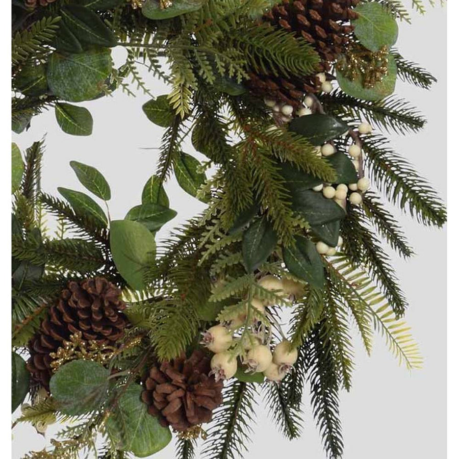 Karácsonyi koszorú, fenyőágakból és eukaliptuszokból, fenyőtobozokkal és fehér erdei bogyókkal díszítve.