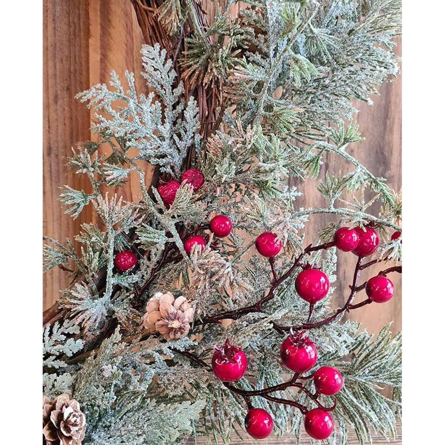 Piros bogyókkal díszített, ezüstös zöld színű mesterséges fenyőágakból készült karácsonyi koszorú, ajtódísz.