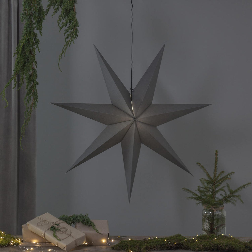 Szürkeszínű, karácsonyi papírcsillag lámpa szürke háttér előtt, fenyőágakkal.
