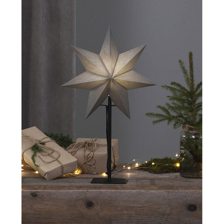 Szürke színű világító karácsonyi papírcsillag, ajándékokkal és fenyőággal.