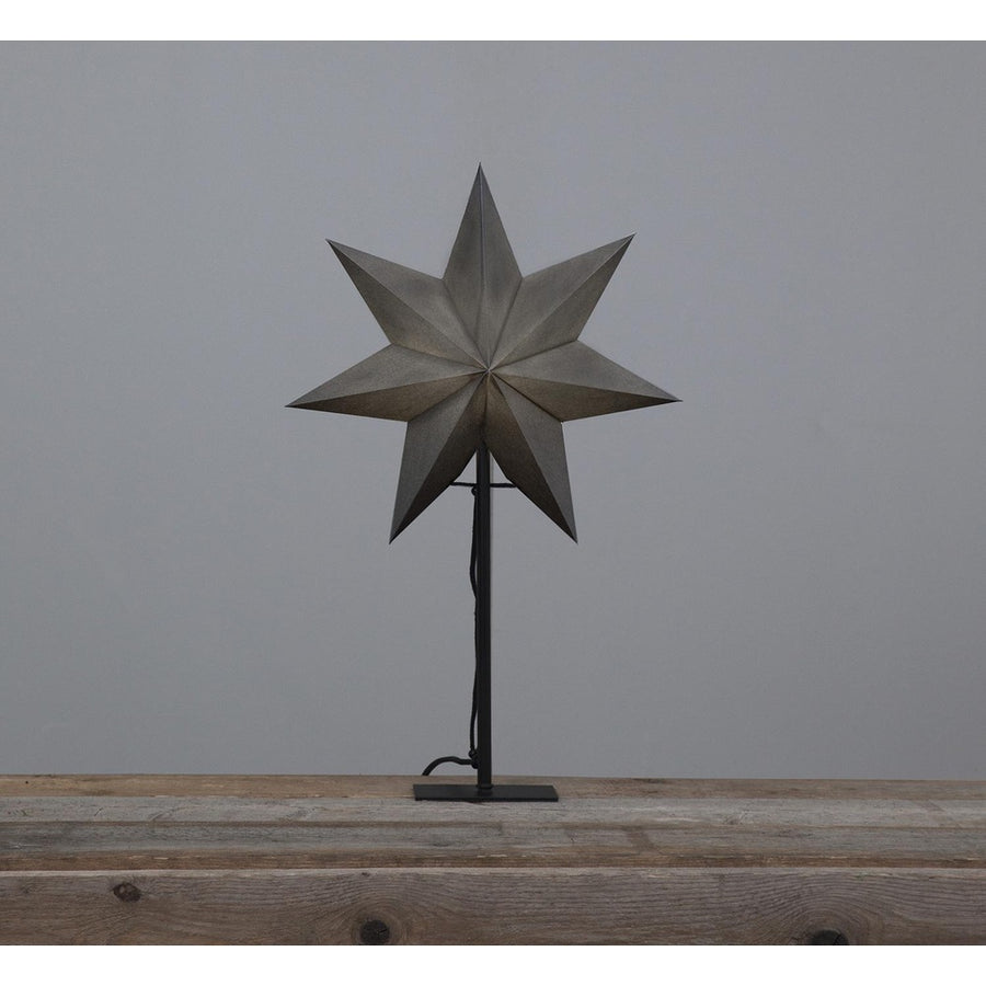 Szürkeszínű karácsonyi pípírcsillag fém talapzaton, natúr fa asztalon.