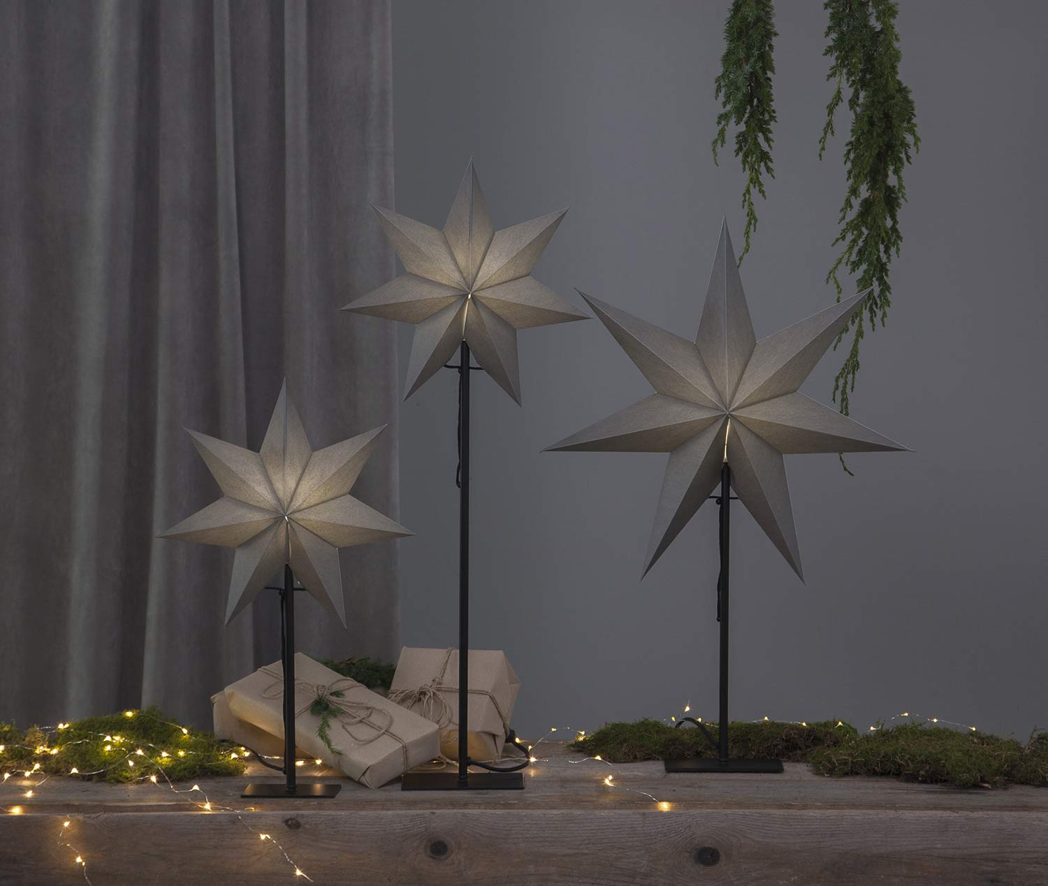 Többféle méretű, szürkeszínű világító karácsonyi papírcsillagok, ünnepi fa asztalon.