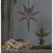 Szürkeszínű, karácsonyi papírcsillag lámpa szürke háttér előtt, fenyőágakkal.