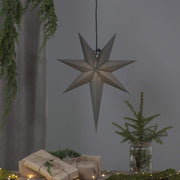 Szürkeszínű, karácsonyi papírcsillag lámpa szürke háttér előtt, fenyőágakkal.