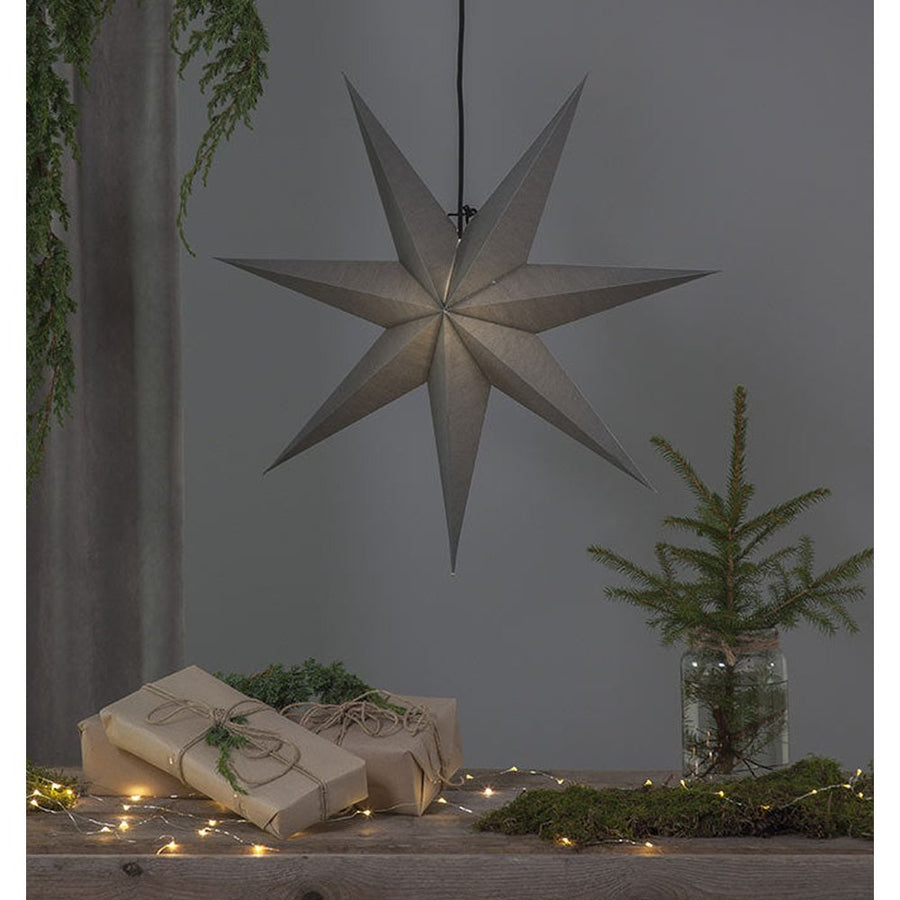 Szürkeszínű, karácsonyi papírcsillag lámpa szürke háttér előtt, fenyőágakkal.
