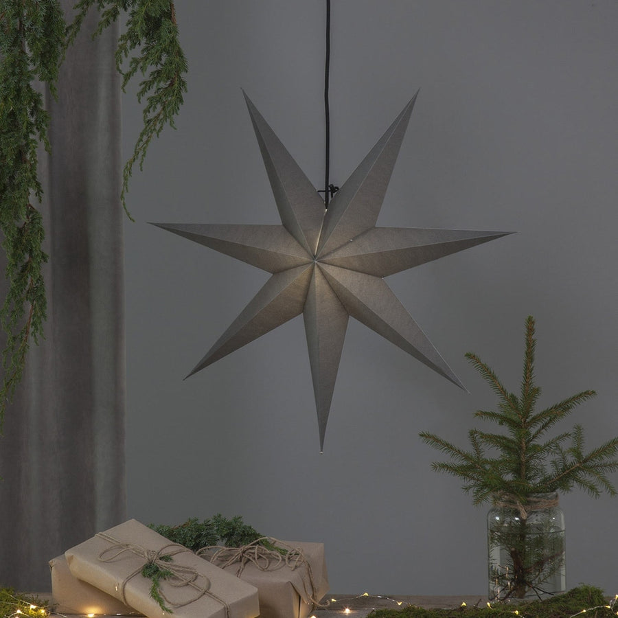 Szürkeszínű, karácsonyi papírcsillag lámpa szürke háttér előtt, fenyőágakkal.
