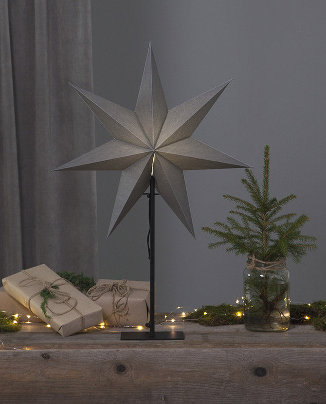 Szürke színű világító karácsonyi papírcsillag, ajándékokkal és fenyőággal.