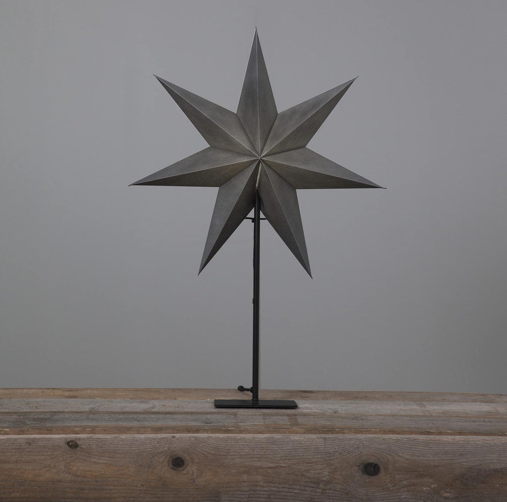 Szürkeszínű karácsonyi pípírcsillag fém talapzaton, natúr fa asztalon.