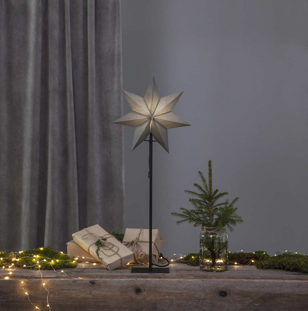 Szürke színű világító karácsonyi papírcsillag, ajándékokkal és fenyőággal.