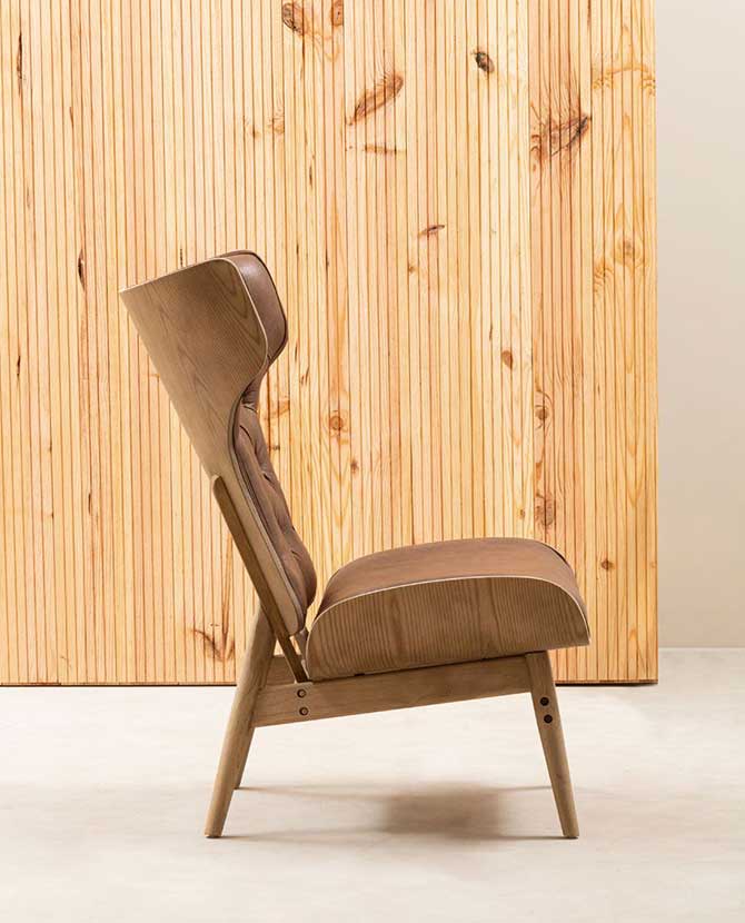 Prémium minőségű, kortárs stílusú, hajlított szilfából készült bőrhatású barna színű bársonnyal kárpitozott szárnyas relaxációs szék oldalnézeti képe natúr színű fa lambéria előtt 
