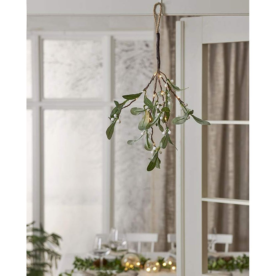 Élethű, 35 cm hosszú, mesterséges fagyöngy ág műnövény, beépített, időzíthető meleg fehér fényű, harmatcsepp formájú LED világítással, fehér ajtótokra kötve  háttérben karácsonyi ünnepi terített asztallal