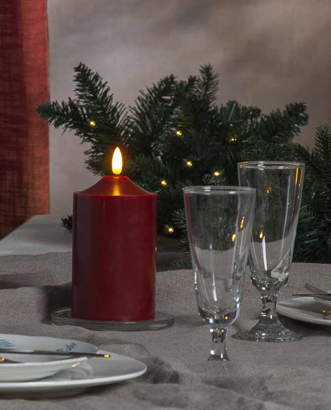 Prémium minőségű, élethű megjelenésű, meleg fehér fényű realisztikus LED lánggal és bordó színű valódi viasztestből kialakított, időzítővel rendelkező 15 cm magas LED oszlopgyertya  ünnepi karácsonyi asztalon üvegpoharakkal 