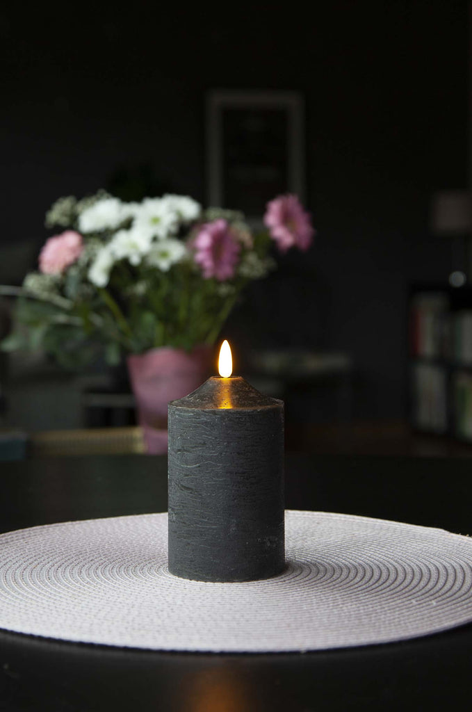 Fekete színű LED gyertya asztalon, virágcsokorral. 