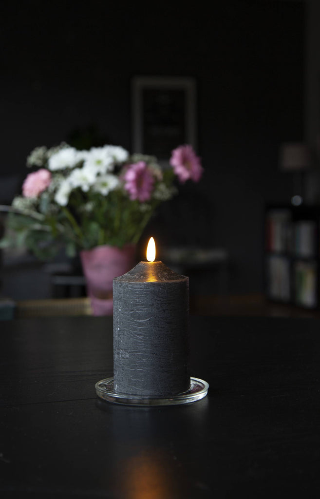 Fekete színű LED gyertya asztalon, virágcsokorral.