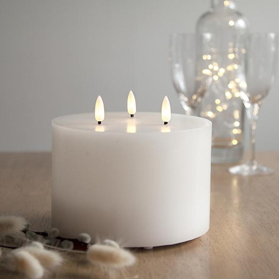 Fehér színű, viaszból készült, 3 darab meleg fehér fényű led lángú led gyertya fa asztalon, barkával az előtérben, háttérben borospohárral