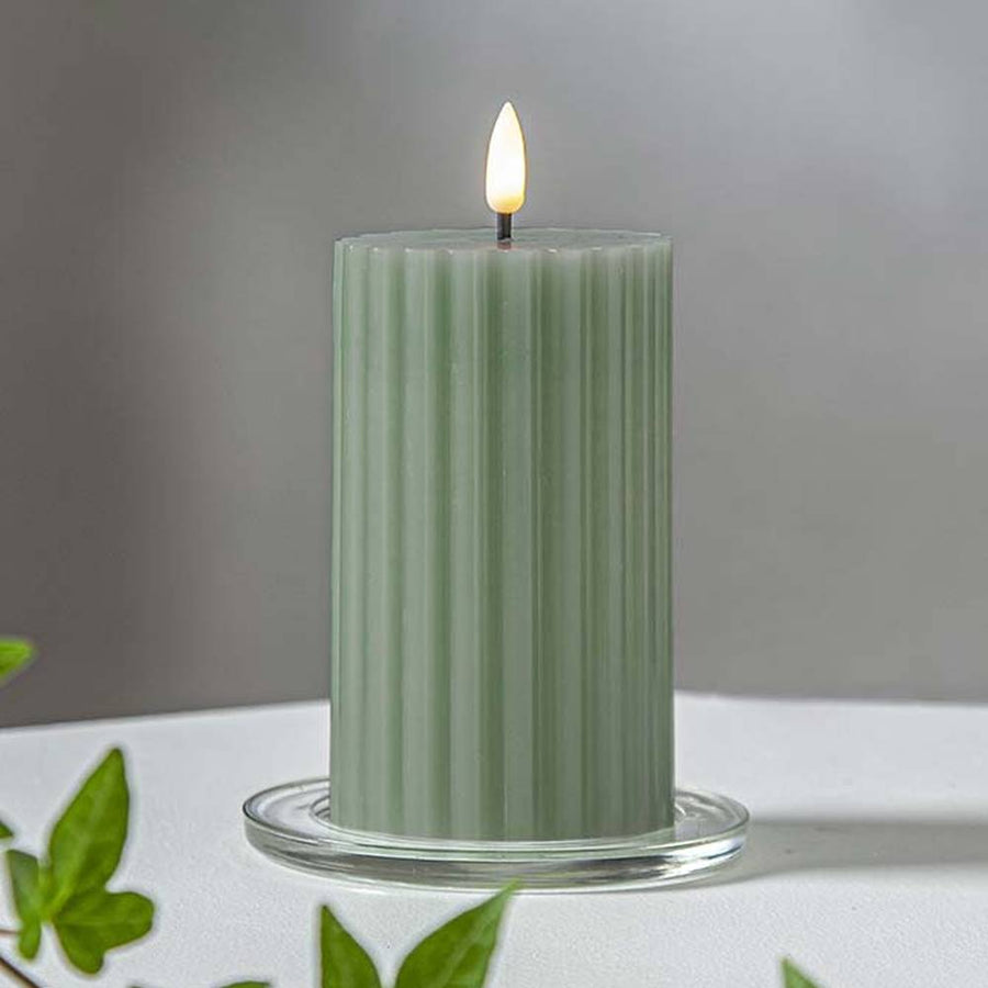 Zöld Stripe LED gyertya dekor pohárban elhelyezve, meleg fényben világítva, zöld növényi elemekkel körülvéve, meghitt beltéri hangulatban.