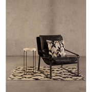 Natúr színű vasból készült, sötétbarna színű marhabőrrel kárpitozott, kortárs-loft stílusú, formatervezett prémium pihenő fotel, dizájn párnával szőnyegen, szürke modern bemutatóteremben, 