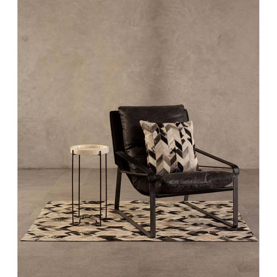 Natúr színű vasból készült, sötétbarna színű marhabőrrel kárpitozott, kortárs-loft stílusú, formatervezett prémium pihenő fotel, dizájn párnával szőnyegen, szürke modern bemutatóteremben, 