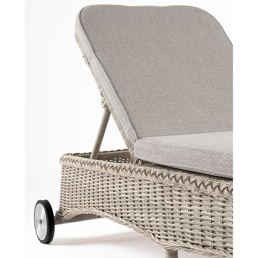 Vidéki vintage stílusú, kerekekkel felszerelt,, dönthető háttámlájú, natúr színű műrattan napozóágy, bézs színű olefin fekvőpárnával,