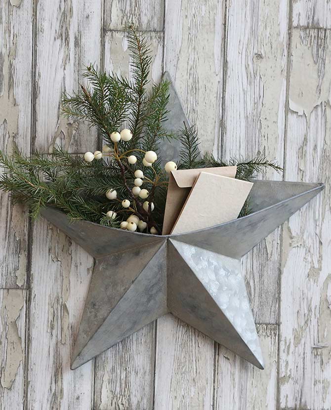 Karácsonyi bádog csillag, rusztikus fehér deszka falon, benne fenyőágak és bogyók. 