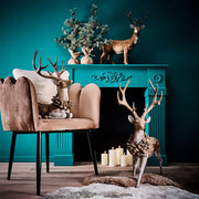 Erdei fenyőtoboz koszorúval díszített, nagyméretű karácsonyi szarvas figura , kék színű szobában, kék kandalló elött.